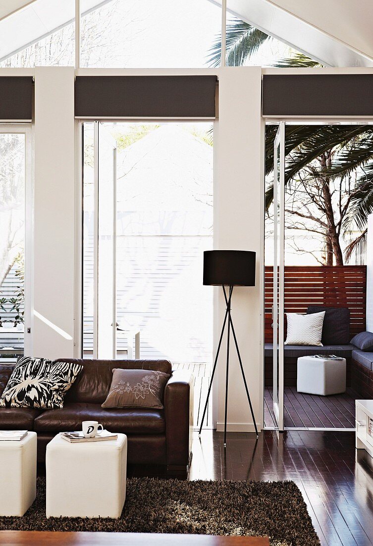 Living room with leather sofa and stained parquet floor; seating area on terrace below palm trees