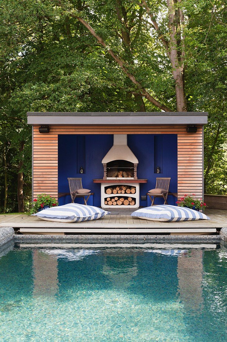 Gekräuselte Wasserfläche auf einem Pool vor schickem Gartenhaus mit gemauertem Grill vor blauer Rückwand