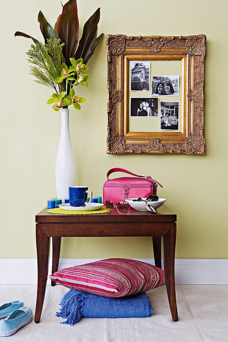 Blumenvase auf antikem Wandtisch und vergoldeter Rahmen mit Photos an pastellgrüner Wand