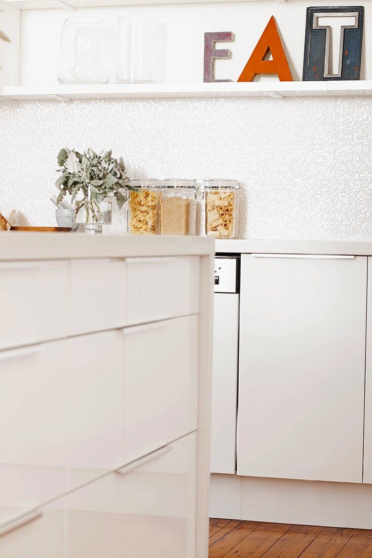 Ausschnitt einer modernen weißen Küche mit Schubladenschrankelement, dekoriertem Wandboard und gefüllten Deckelgläsern auf der Arbeitsplatte