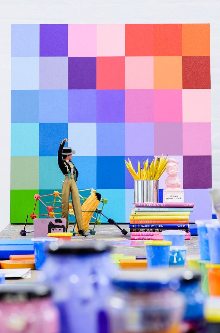 Sänger-Figur, Bücher und Farbtöpfe vor Farbmustertafel an Wand