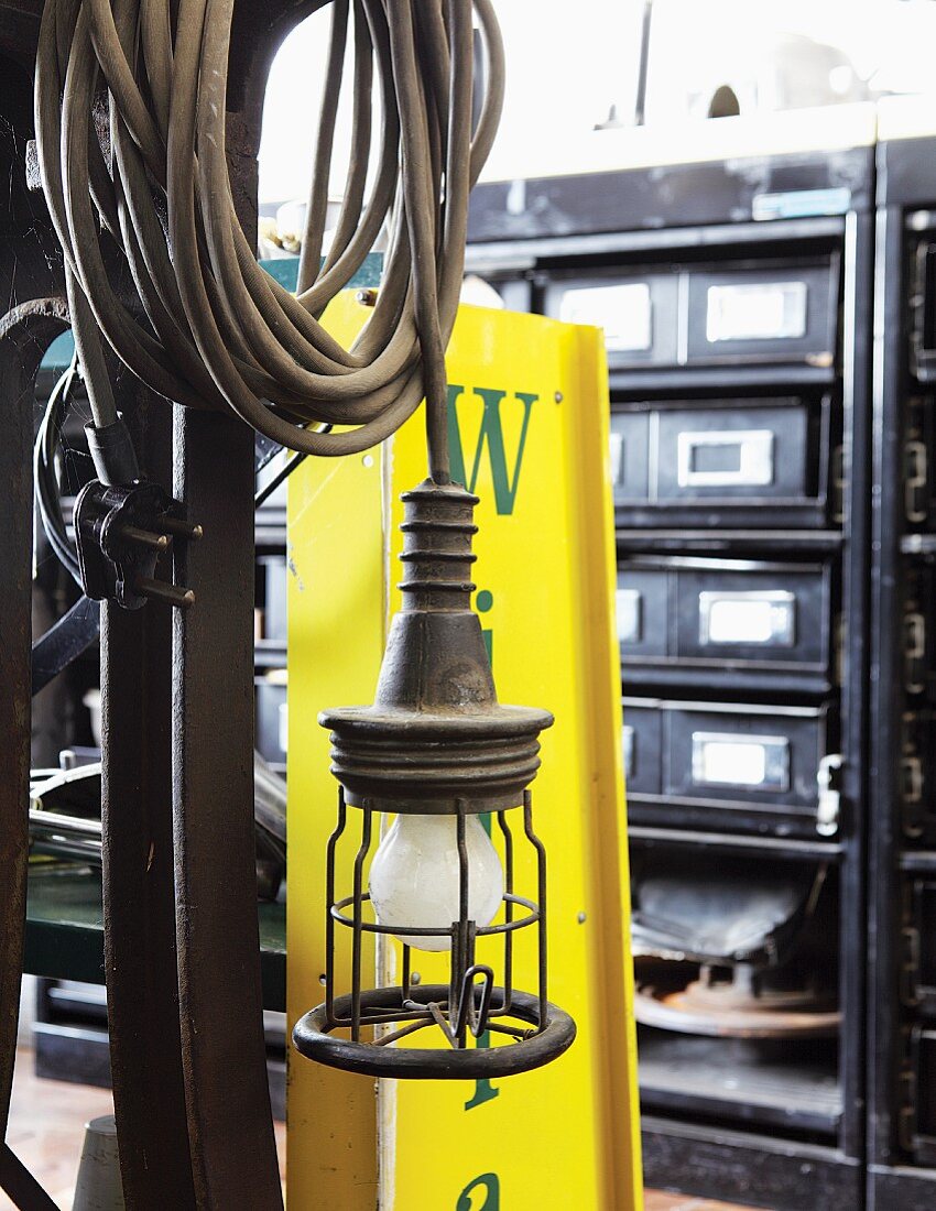 Vintage lamp with coiled cable and yellow, sheet metal advertising panel in front of chest of drawers