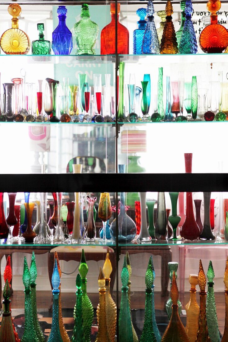 Collection of coloured glass bottles and vases on glass partition shelving