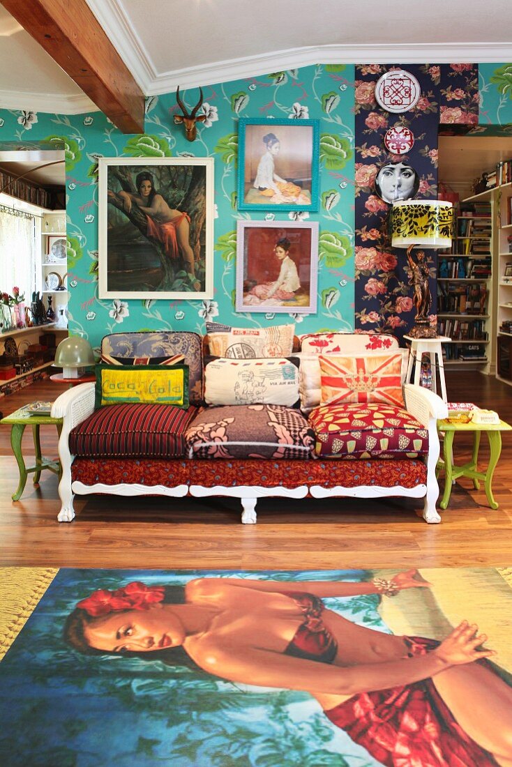 Cushions covered with various textiles on sofa, rug with picture of woman and pictures on wall with patterned wallpapers