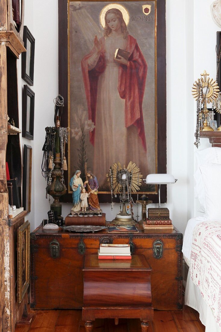 Arrangement of devotional objects and ornate monstrance on trunk below large painting of a Madonna