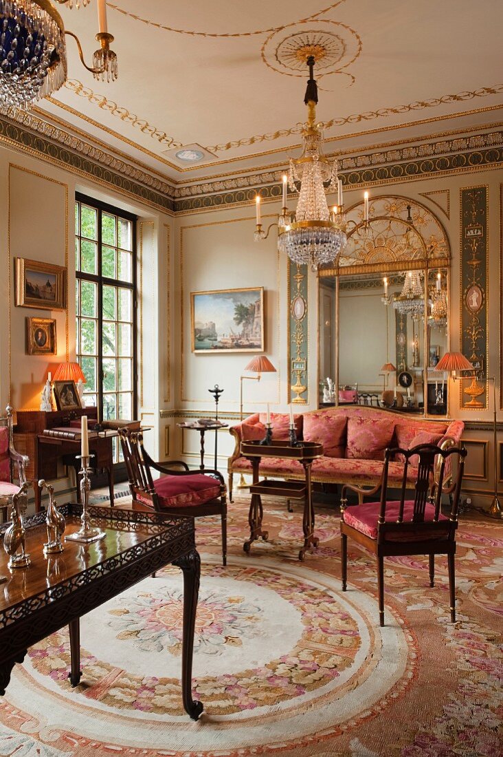 Mahogany table and chairs and antique upholstered sofa on Aubusson rug in stylish salon of Georgian apartment in London
