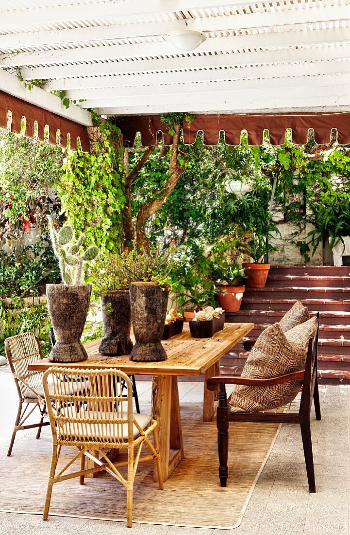 Roofed terrace seating area with potted plants on table in front of exterior steps
