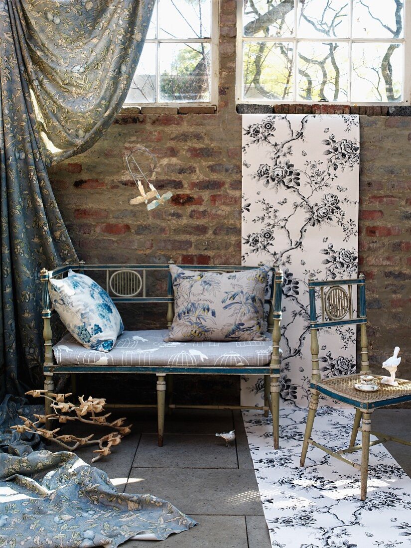 Elegant Rococo bench and chair with unrolled length of wallpaper on brick wall and floor