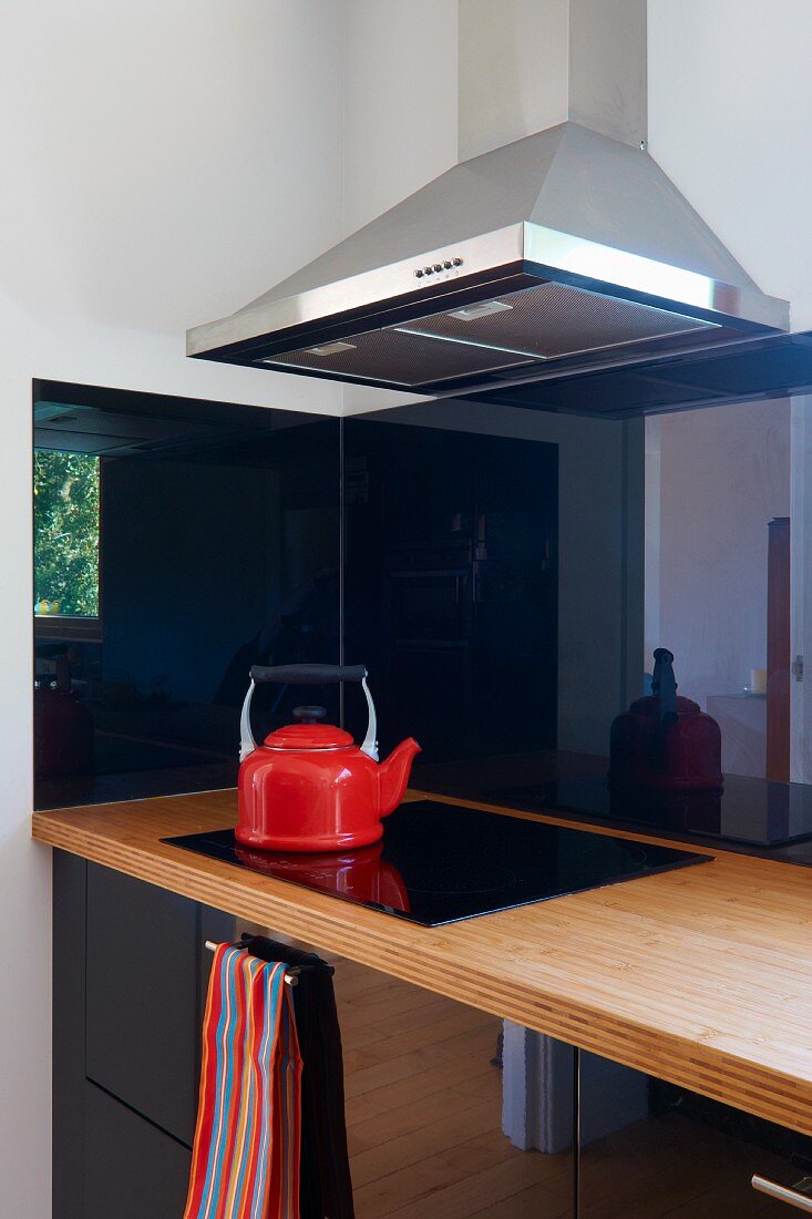 Ecke einer modernen Küche mit reflektierenden Fronten in Schwarz; auf dem schwarzen Ceranfeld ein roter Wasserkessel