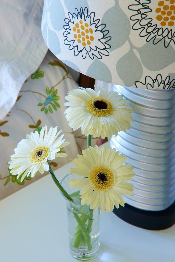 Modern bedside lamp with floral lampshade next to small vase of gerbera daisies