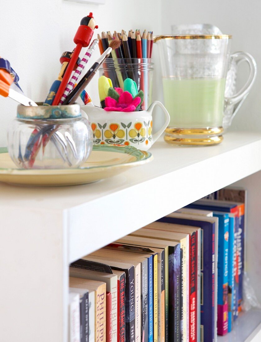 Containers of writing utensils on white bookshelves