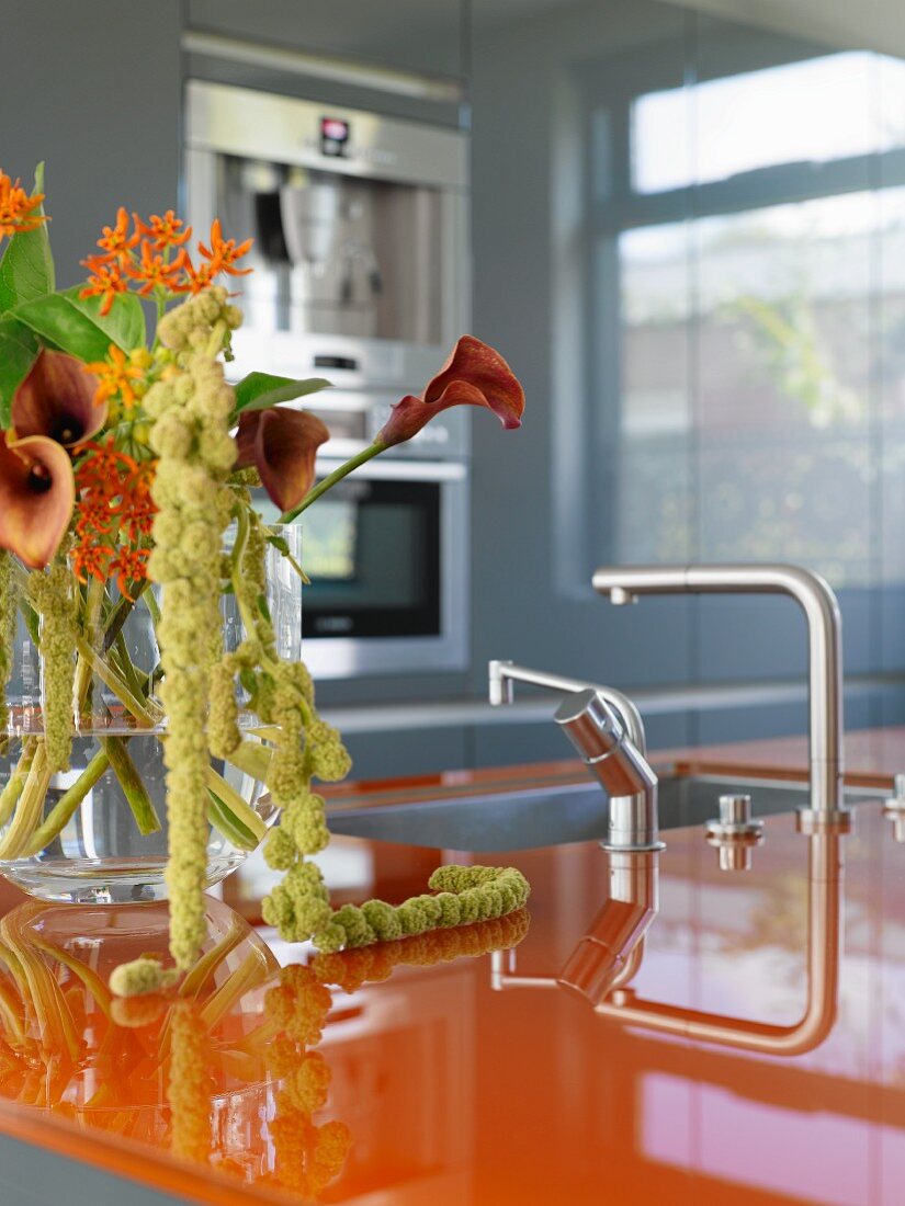 Designer kitchen with orange worksurface and bouquet of calla lilies in glass vase