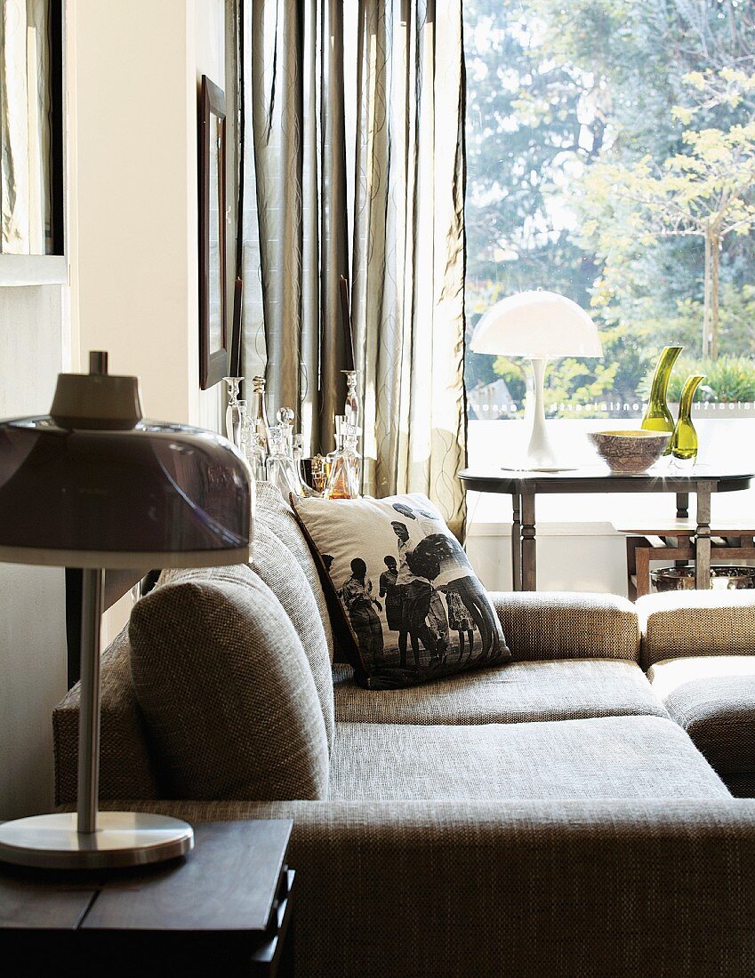 Comfortable sofa and side table with table lamp in front of window with view of garden