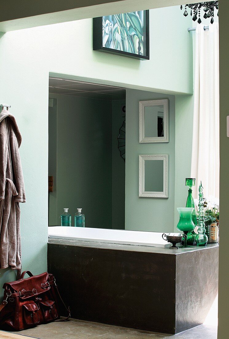 Free-standing, modern bathtub partially built into niche in bathroom painted pale green