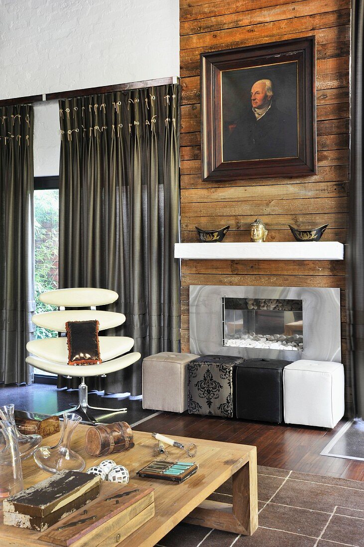 Oil portrait on rustic wooden panelling above fireplace, cubic pouffes of different colours and wooden coffee table