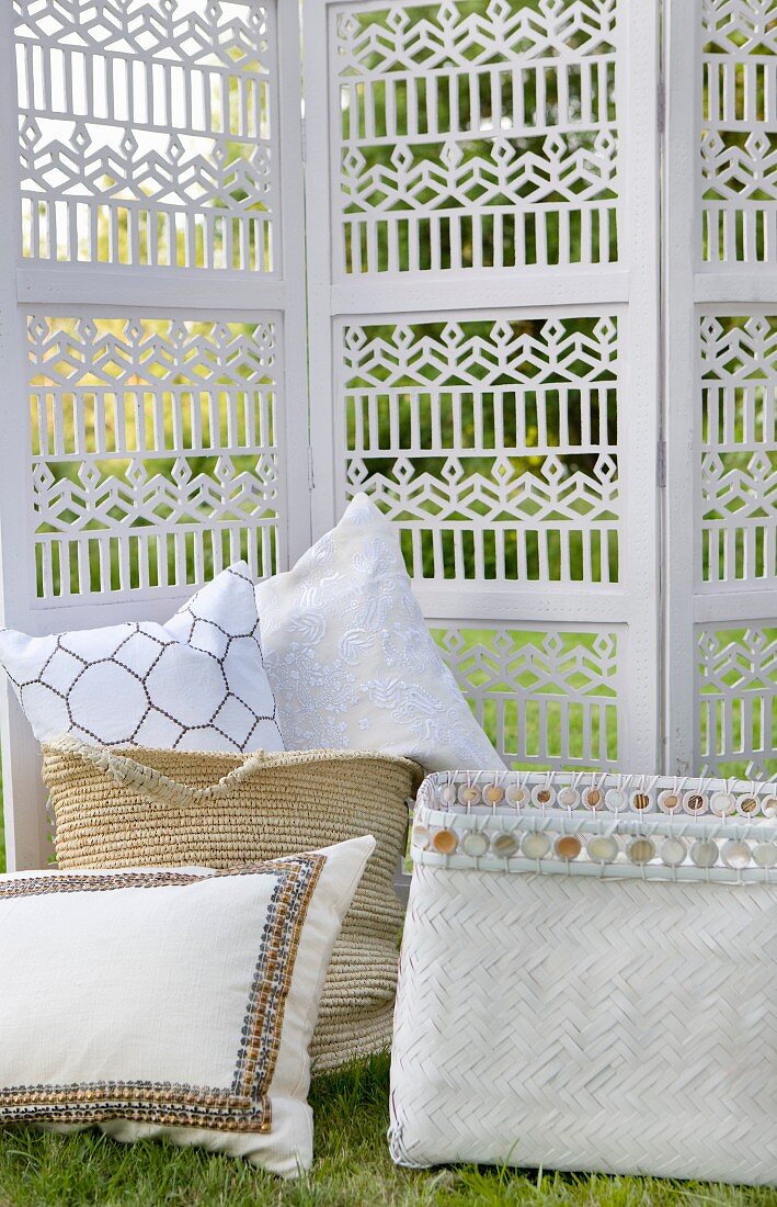 Cushions in baskets in front of carved screen in garden