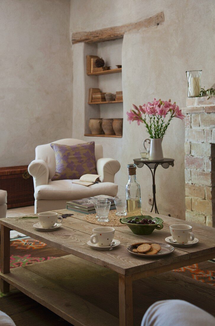 Wooden coffee table in front of fireplace; country-house armchair and shelves of ceramics in niche in background