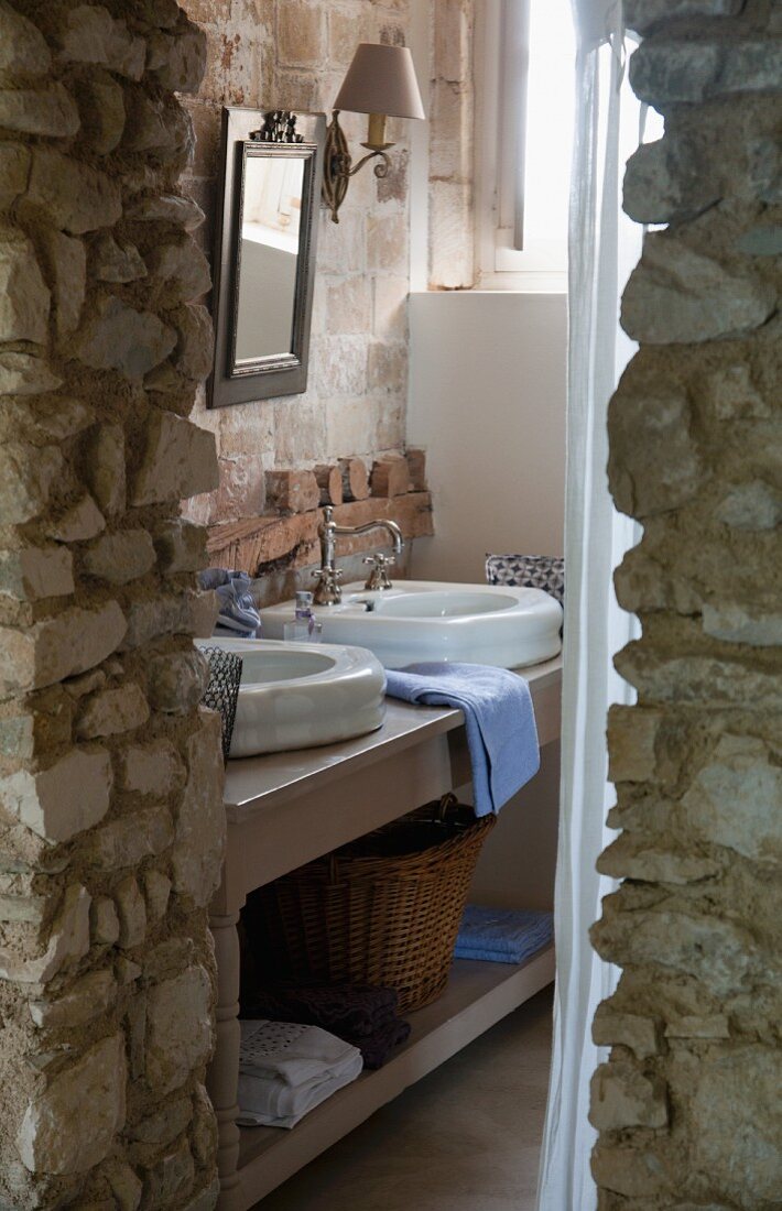 View past rustic stone wall of washstand with twin basin in bathroom