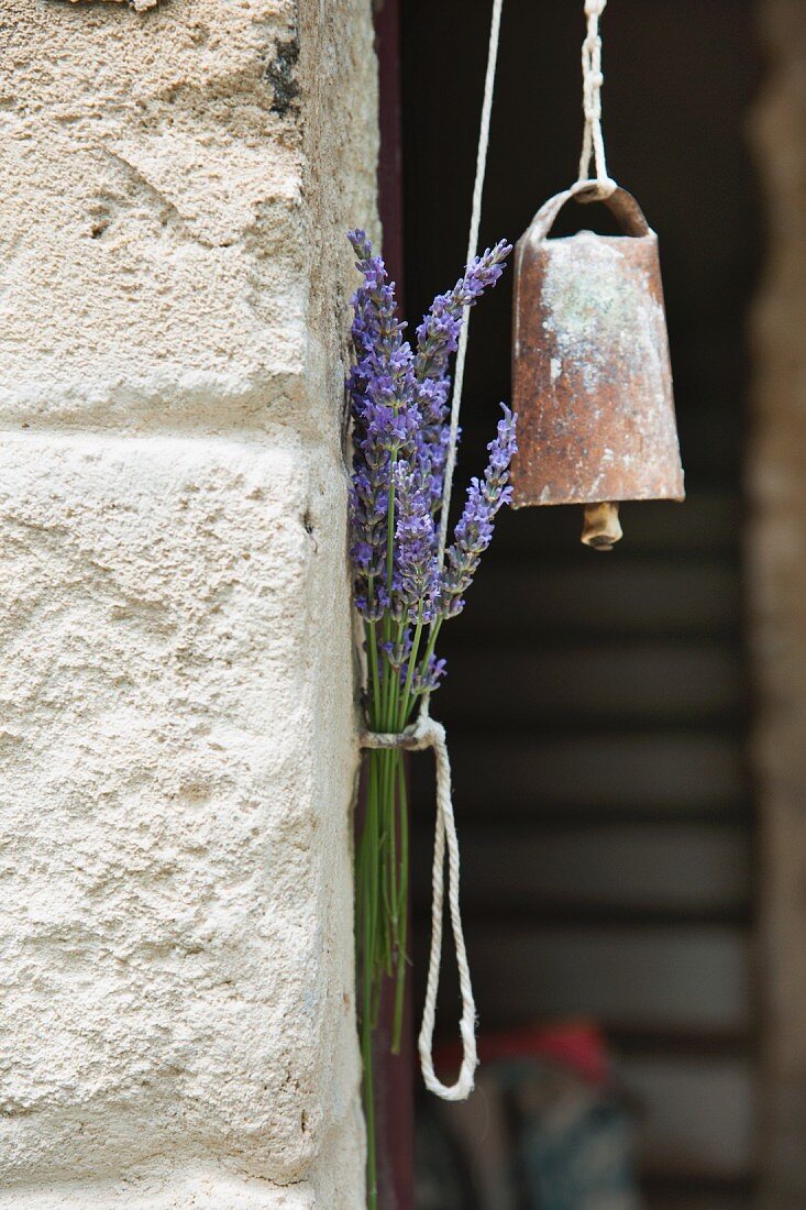 An Schnur aufgehängte alte Glocke und Lavendelstrauss am Gemäuer