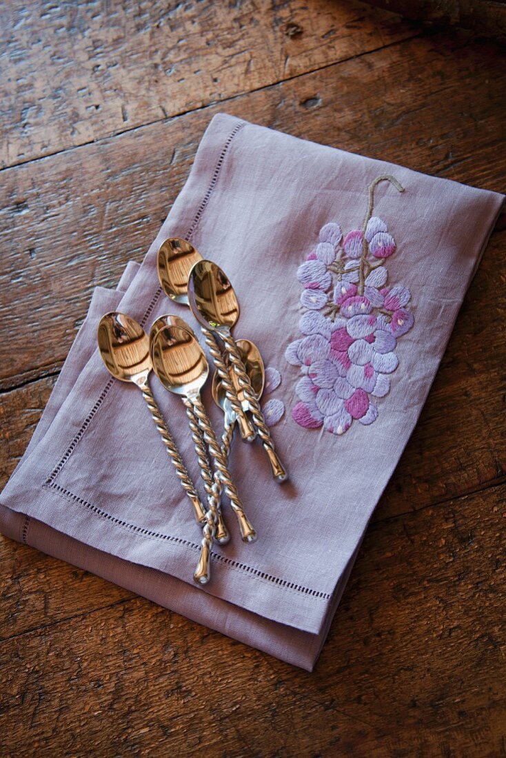 Silver spoons with twisted stems on embroidered linen napkin on old wooden table