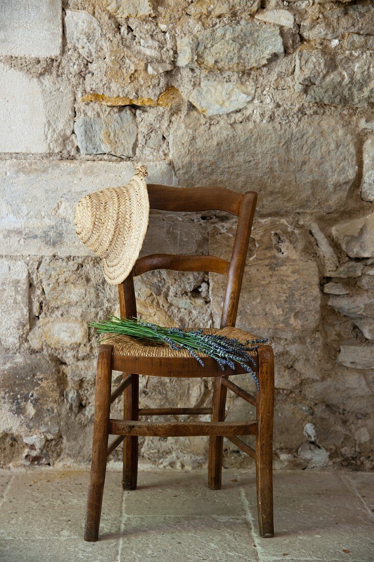 Straw hat and bouquet of lavender on Mediterranean, rush bottom chair against stone wall