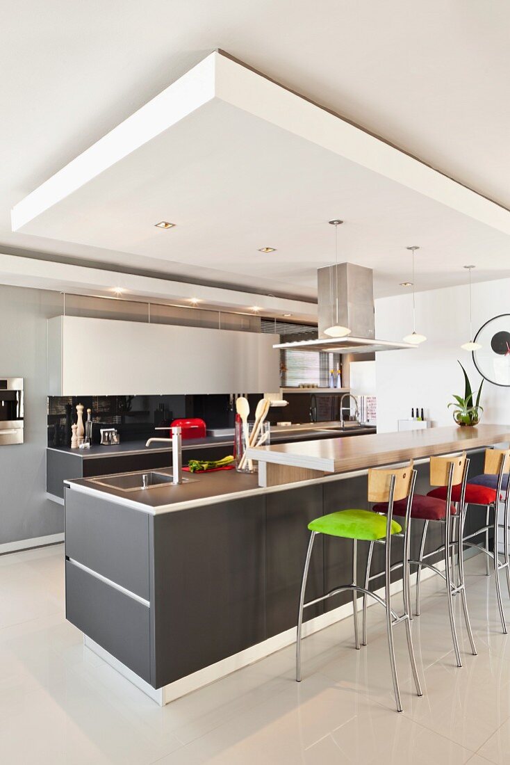 Küchenblock mit grauer Oberfläche und Barhocker mit farbigem Polsterbezug in offener Küche