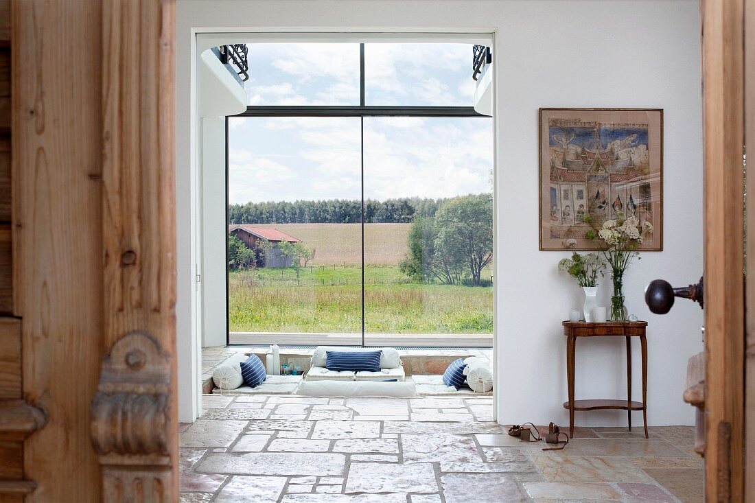 Blick durch geöffnete Eingangstür in Flur und Wohnzimmer eines modernen Landhauses mit Panoramafenstern