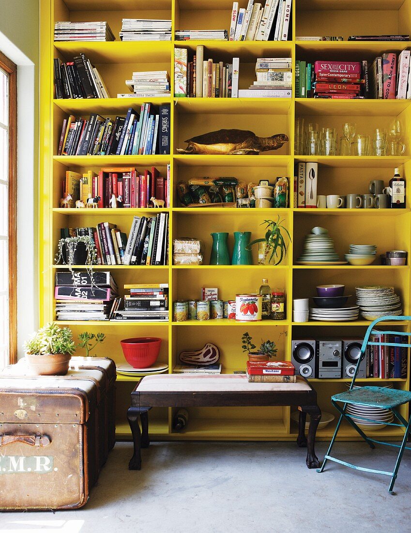 Couchtisch neben Vintage Truhe aus Leder vor gelb lackiertem Regalschrank mit Geschirr und Büchern