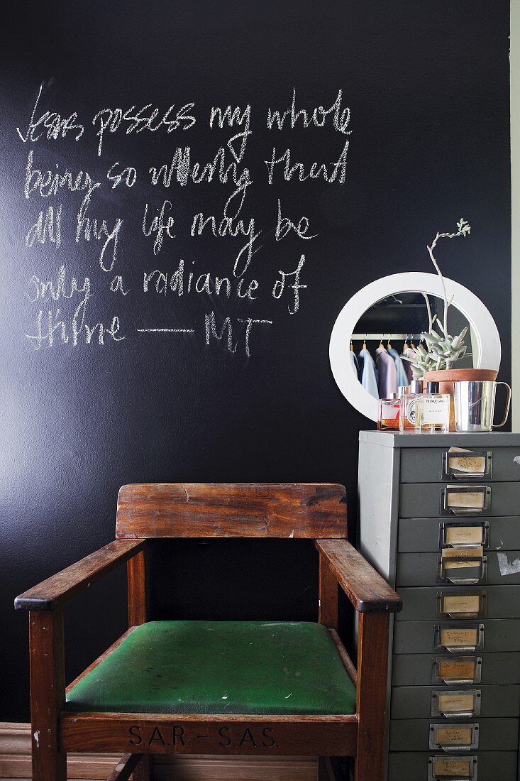 Wooden chair with green seat cushion and vintage-style, metal office cabinet in front of black chalkboard