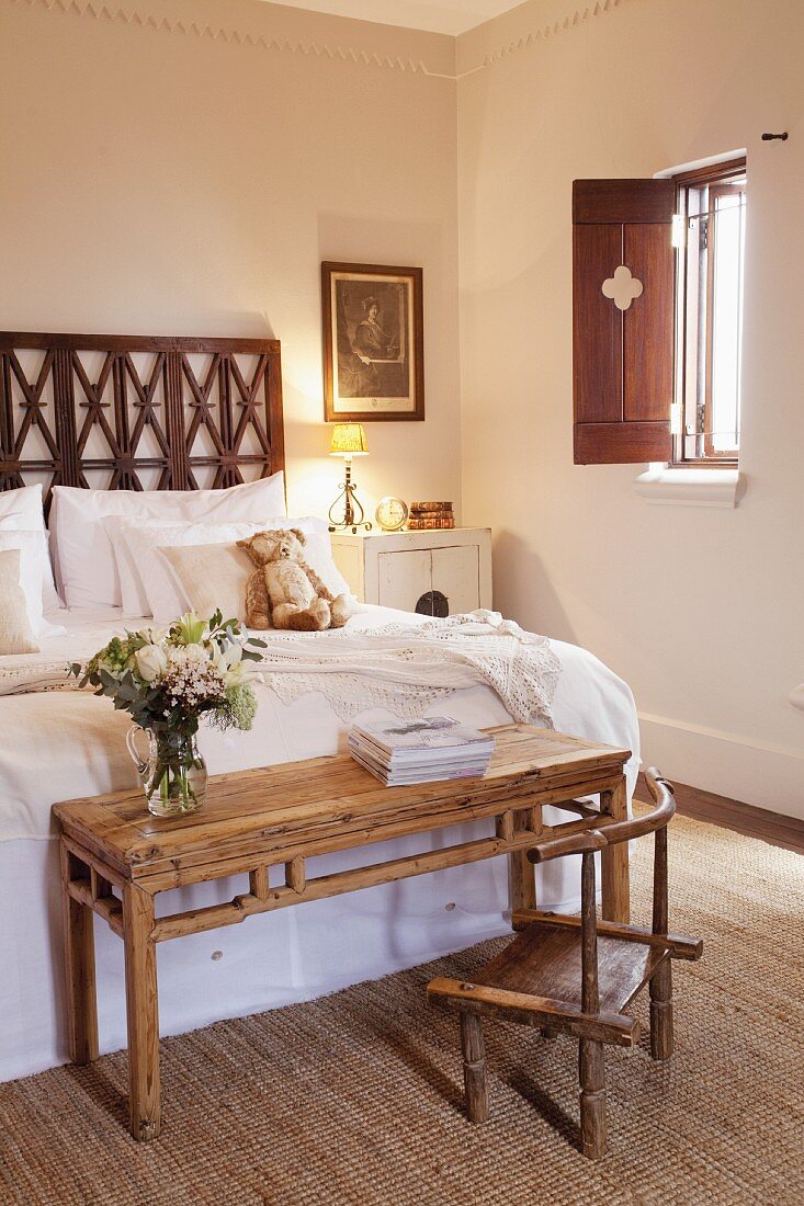 Schlafzimmer mit marokkanischem Flair; am Fussende des Bettes ein einfacher Holztisch mit rustikalem Stuhl