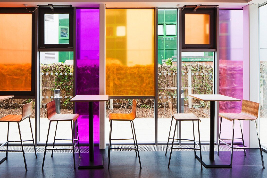 Stehtische und Barhocker vor Glasfassade mit farbigen Glaspaneelen