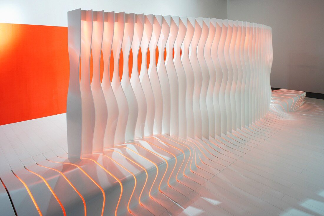 Raumteiler aus geformten Lamellen mit integrierter Bank vor Wand mit oranger Farbfläche