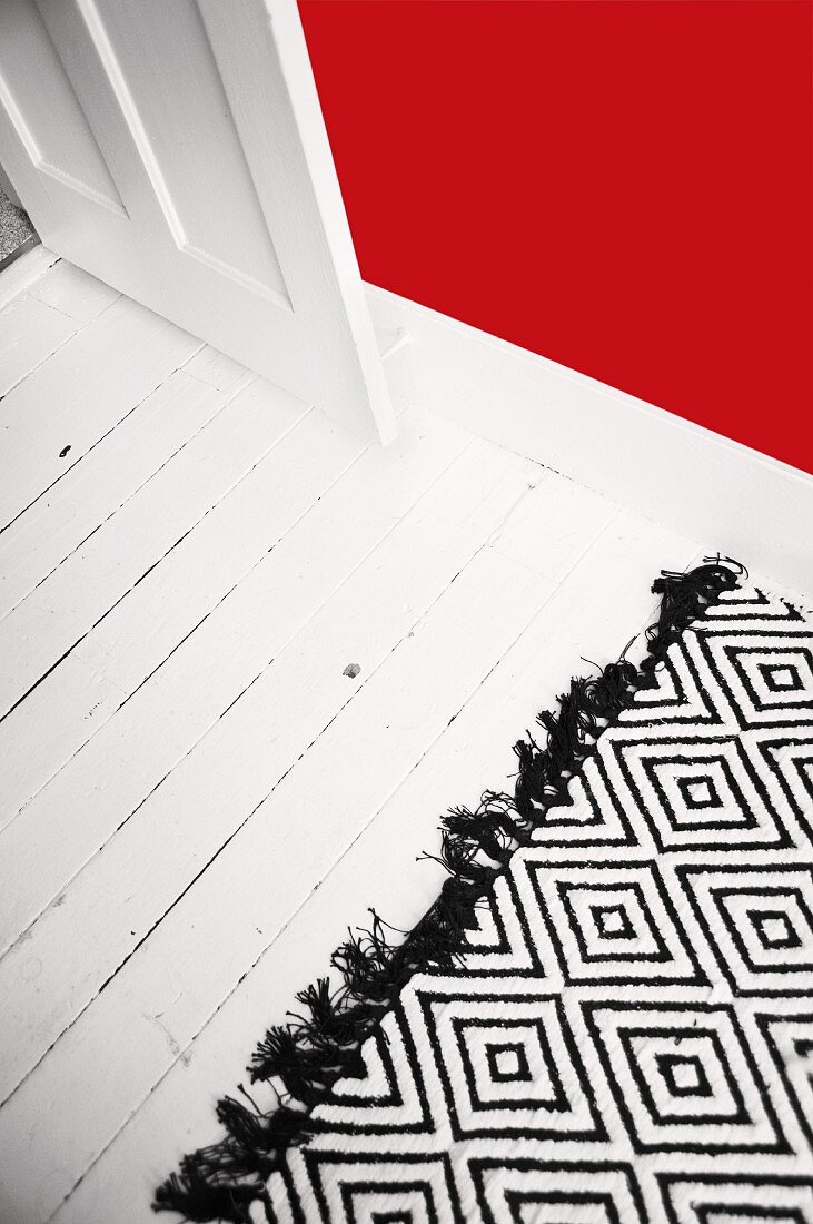 Weiß lackierter, alter Holzdielenboden mit schwarz-weißem Wollteppich und roter Wand