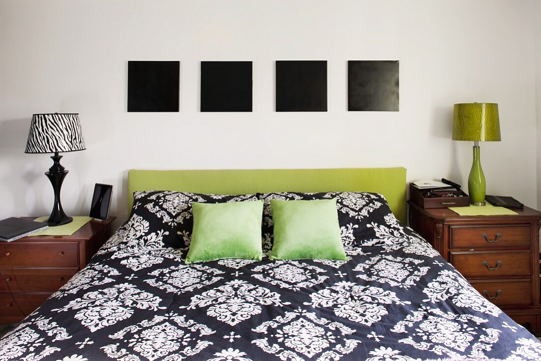 Double bed with headboard upholstered in olive green below four square, monochrome black pictures