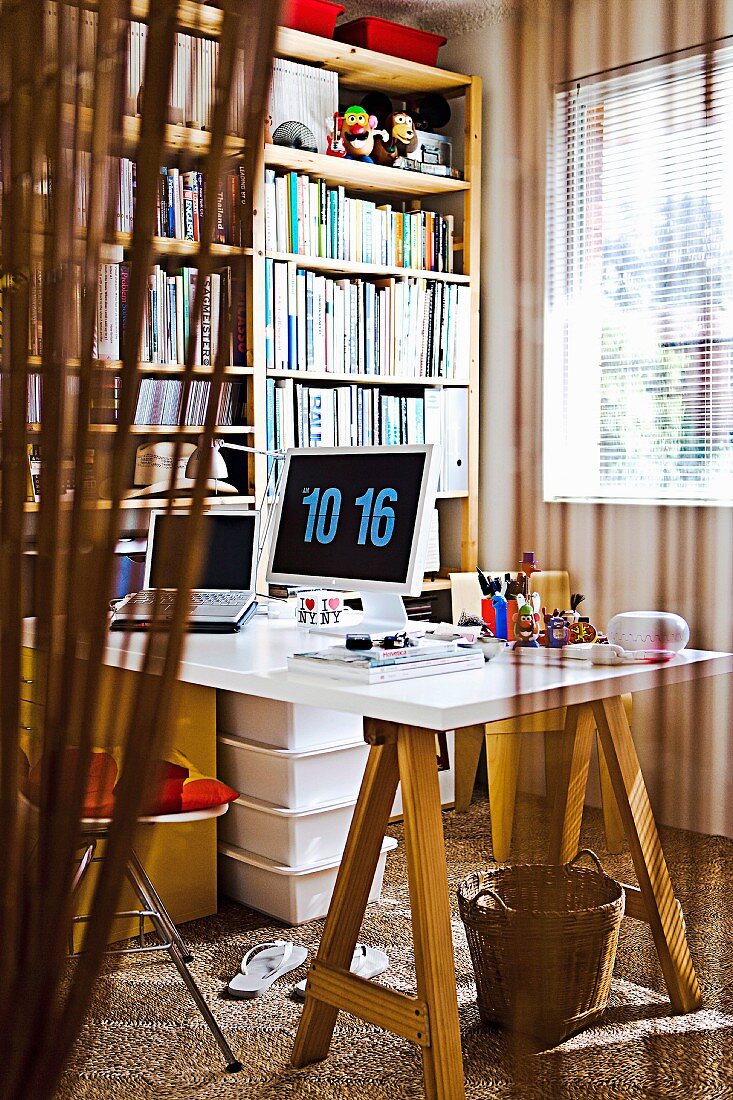 Blick in Arbeitszimmer mit einfachem, aufgebocktem Schreibtisch und großer Bücherwand
