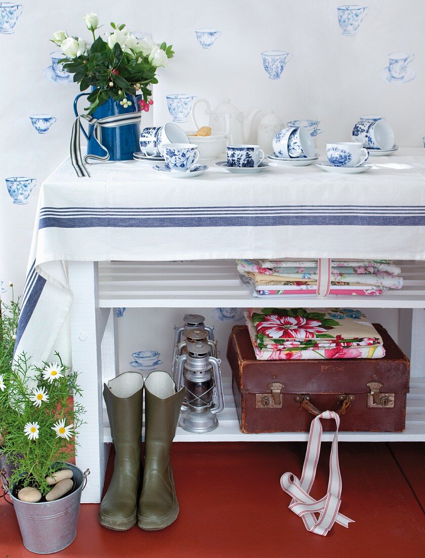 Klassisches blau-weisses Geschirr auf einem Regal und als Dekomotiv auf der Wand; floral gemusterte Stoffe und Vintagekoffer