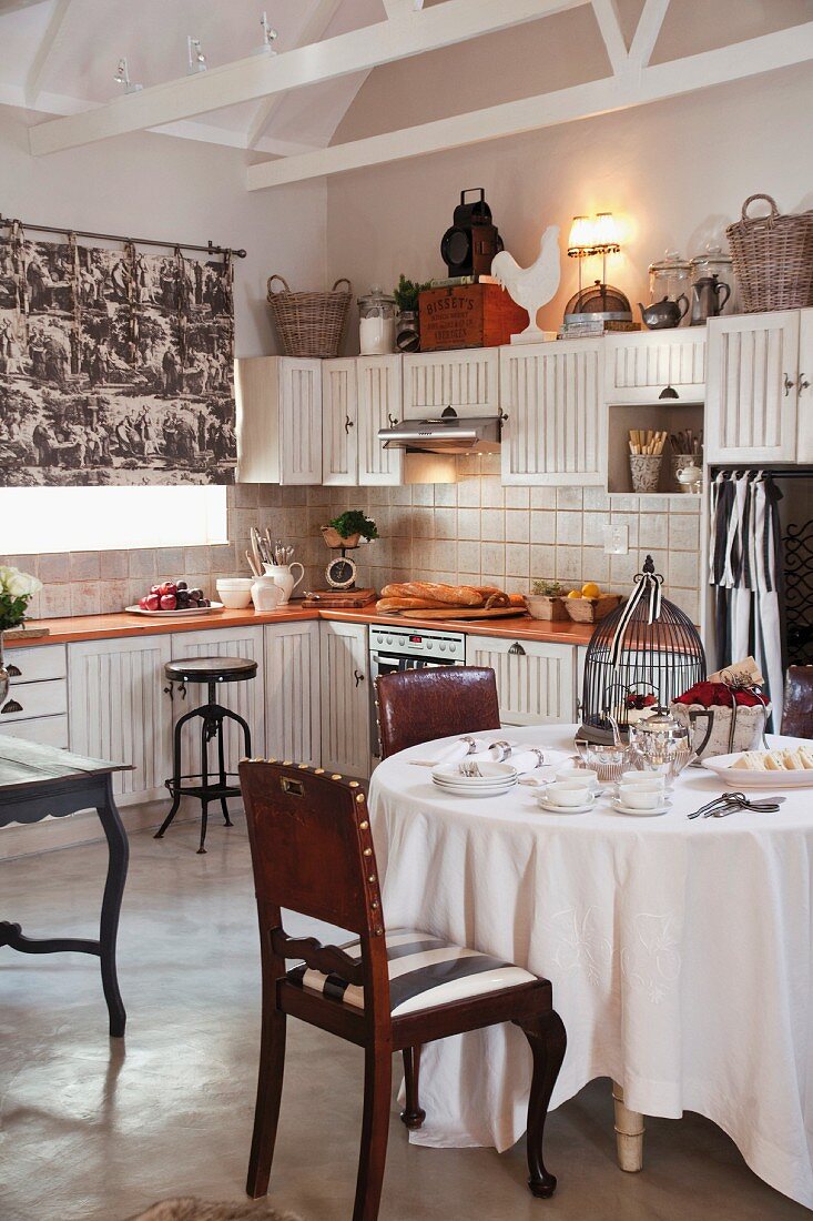 Country-house-style kitchen with antique leather chairs around set table with white tablecloth