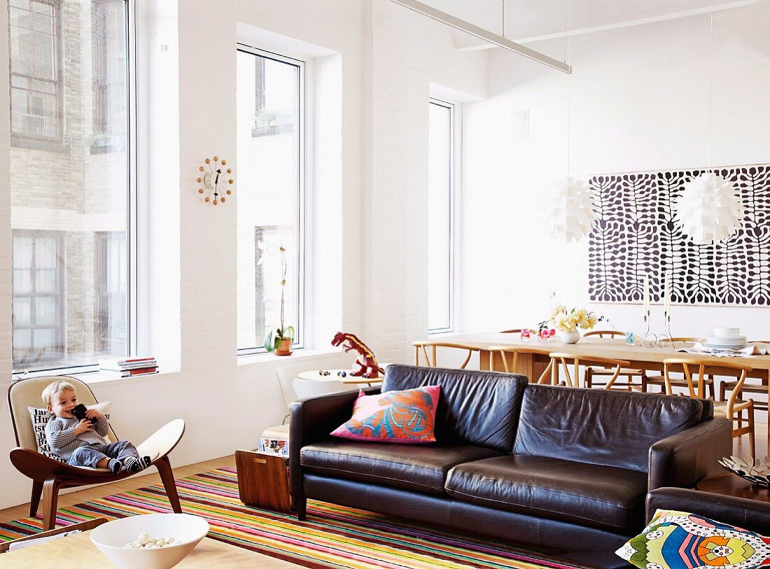 Offener gemütlicher Wohnraum eines Lofts mit Designermöbeln und Kleinkind im Sessel