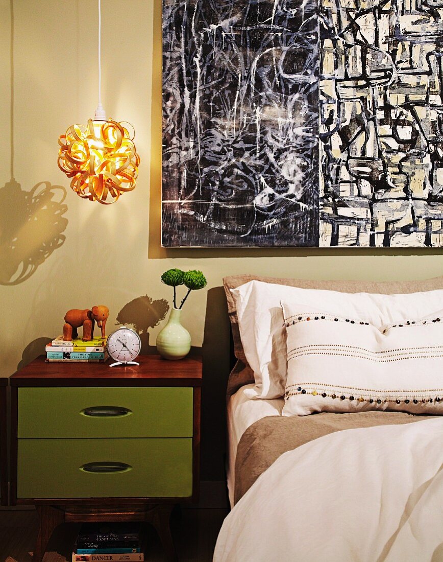 Schlafzimmer mit grünem Nachtkästchen und oranger Pendelleuchte, daneben moderne Malerei