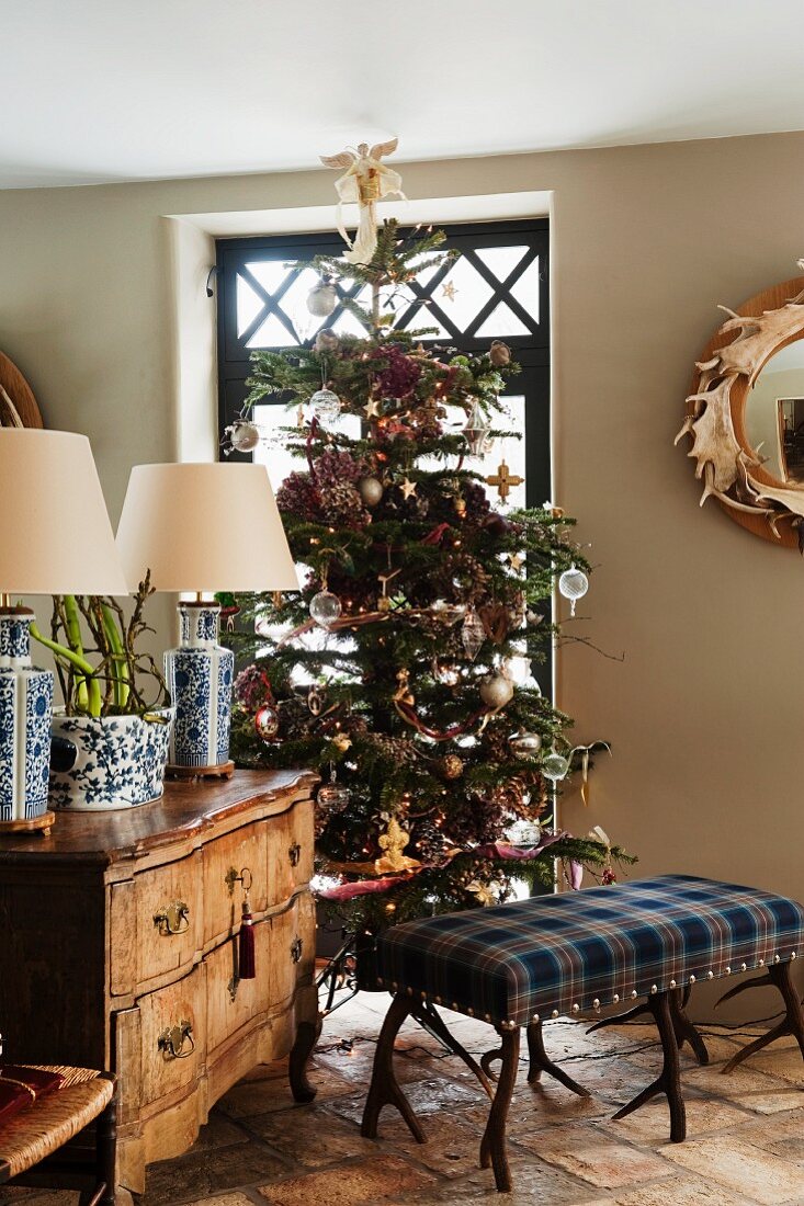 Im Tartanmuster bezogene Polsterbank mit Geweihfüssen vor geschmücktem Weihnachtsbaum und antiker Kommode in englischem Wohnzimmer