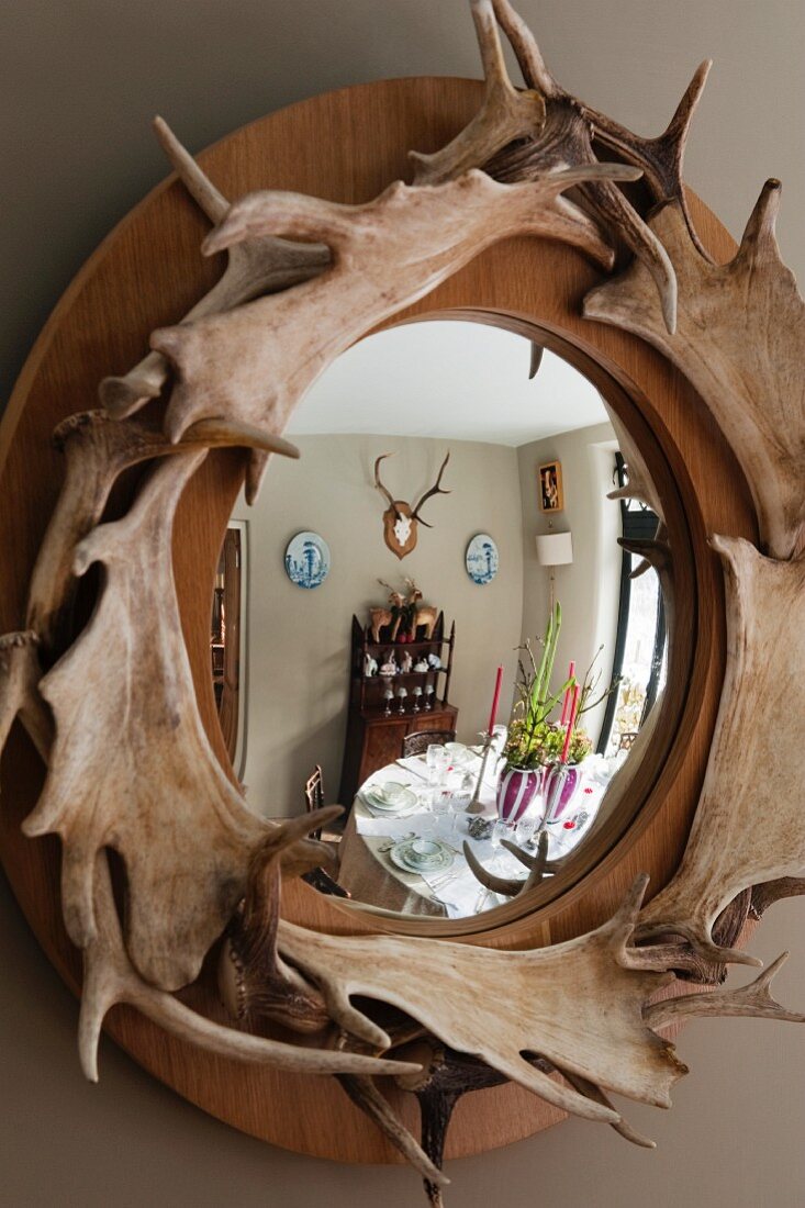 Festively set dining table reflected in mirror with wooden frame decorated with antlers