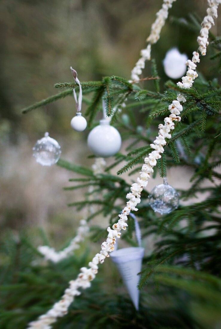 Weisser Weihnachtsschmuck und Popcorngirlande an Tannenbaum im Freien
