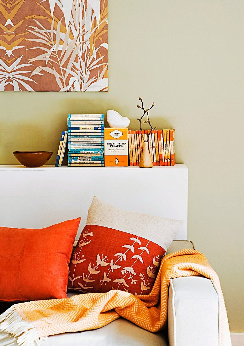 Day bed with pillows and bedspread in orange tones; behind it a white book board