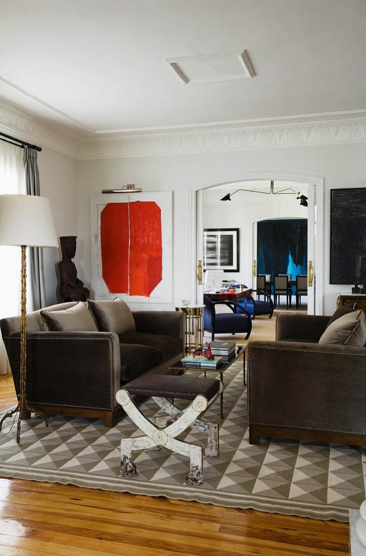 Klassische Sofagarnitur mit grauem Samtbezug und Hocker mit Metallgestell in herrschaftlichem Wohnzimmer mit modernen Bildern an Wand
