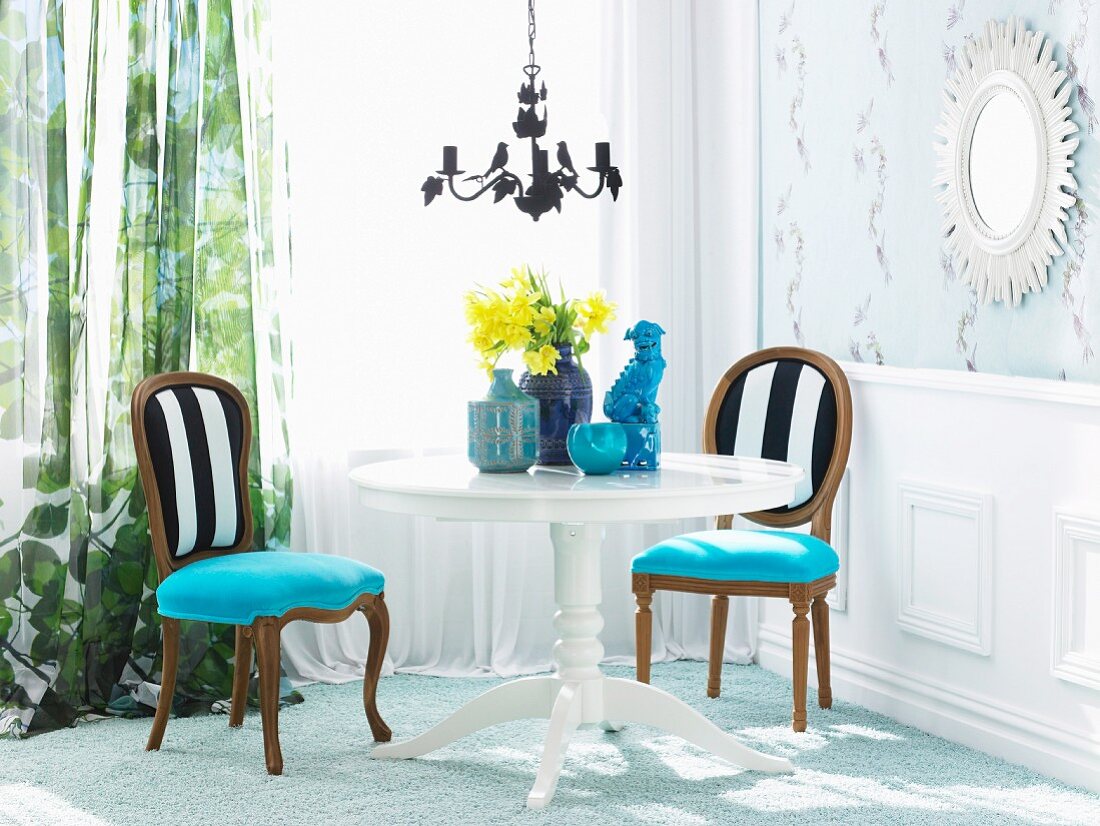 Elegante Wohnzimmerecke im traditionellen Stil mit weißem runden Holztisch, darauf blaue Keramikkunstobjekte und Narzissenstrauss