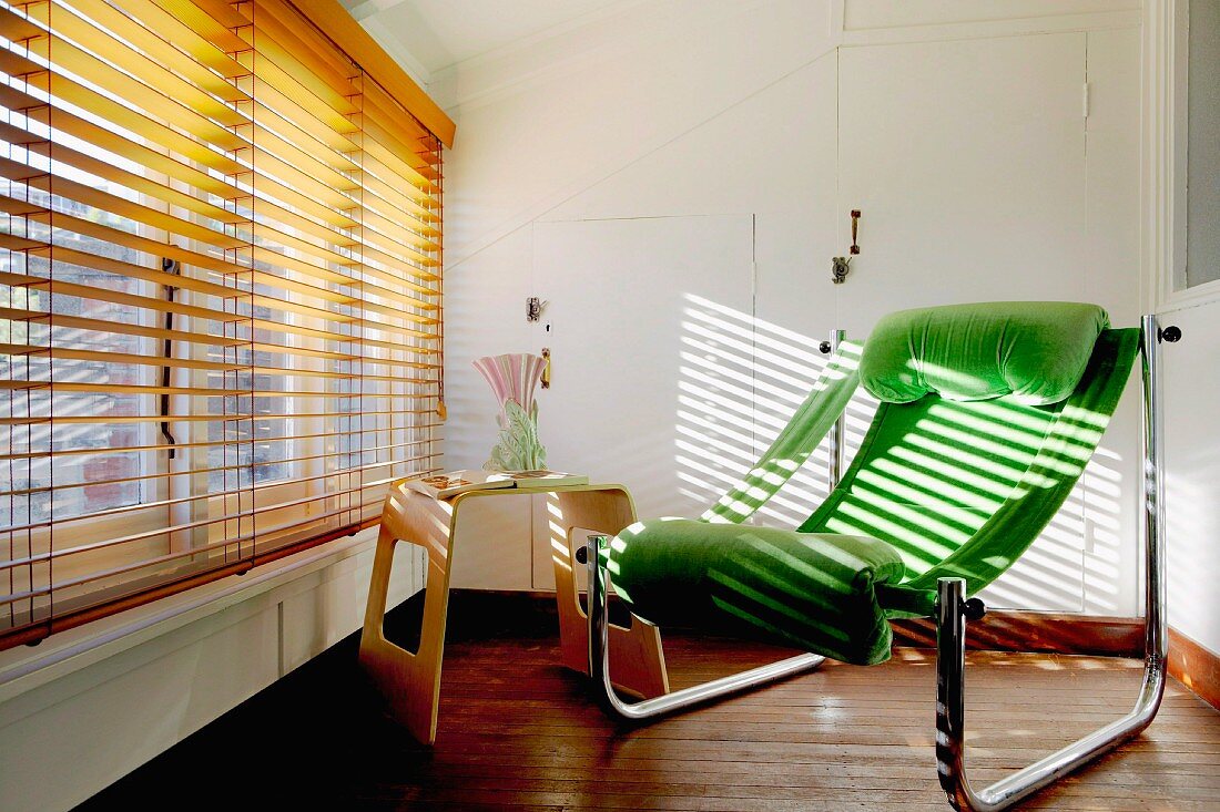 Green lounger and side table in front of large window with venetian blind