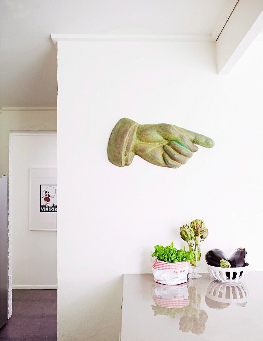 Handskulptur mit ausgestrecktem Zeigefinger an weisser Wand über der Küchentheke