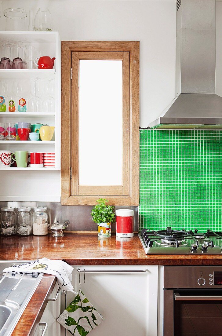 Küchenfenster neben grün gefliester Wand und Küchenregal mit diversem Geschirr