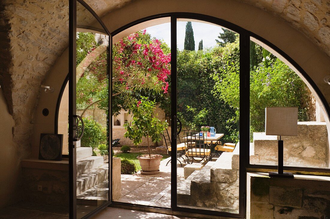 Blick in sonnigen, mediterranen Innenhof durch halbkreisförmige Fensterfront