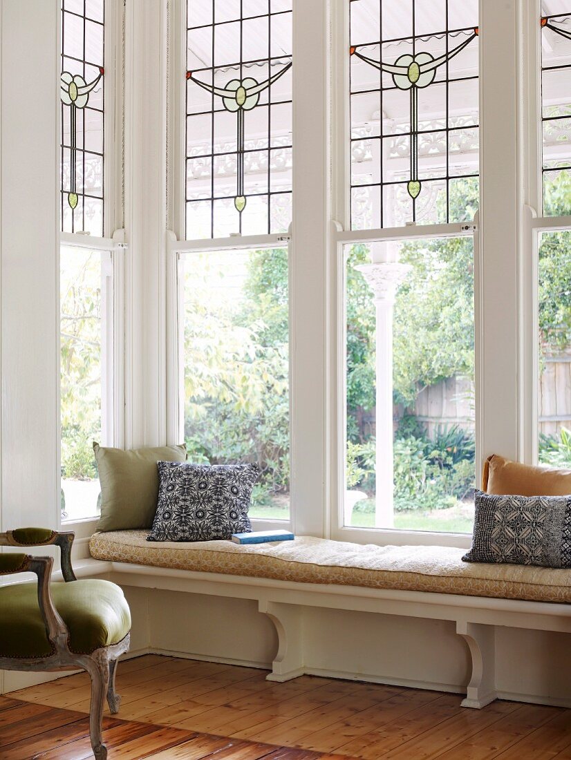 Wooden bench with pad in front of tall bay windows with traditional, lead glazed windows